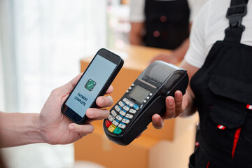 Asian Couple paying while unloading boxes and furniture from a pickup truck to a new house with service cargo two men movers worker in uniform lifting boxes. concept of Home moving and delivery.