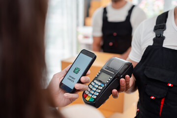 Asian Couple paying while unloading boxes and furniture from a pickup truck to a new house with service cargo two men movers worker in uniform lifting boxes. concept of Home moving and delivery.