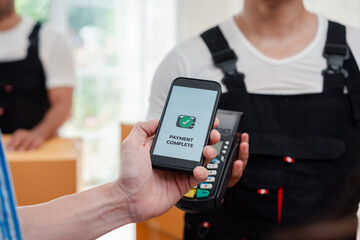 Asian Couple paying while unloading boxes and furniture from a pickup truck to a new house with service cargo two men movers worker in uniform lifting boxes. concept of Home moving and delivery.