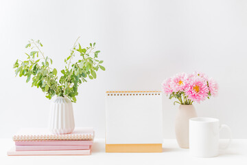 Mockup white desk calendar and pink flowers in a vase on a light background. Spiral calendar for...