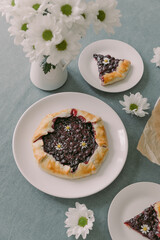 A whole biscuit on a white plate in the center of the frame. Near by two plates with sliced ​​biscuits.On the table is a turquoise tablecloth. .On the table is a vase with daisies. Top shooting point.