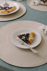 A piece of currant biscuit on a white plate, which stands on a beige placemat. There is a turquoise tablecloth on the table. in the background are white plates on which are pieces of biscuits.