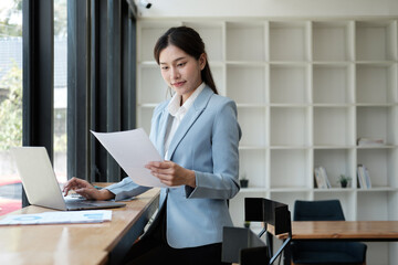 Smart and pretty young Asian businesswoman holding paper, analyzing information from the document, preparing for the next project.
