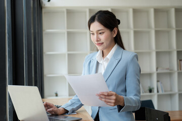 Smart and pretty young Asian businesswoman holding paper, analyzing information from the document, preparing for the next project.