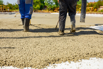 Riggers, workers use rake and handmade wooden tool to level fresh concrete into building foundation
