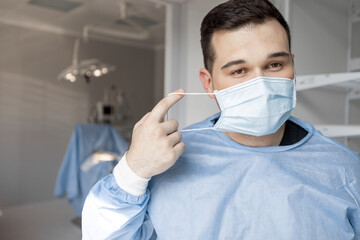 Portrait of a tired surgeon taking off his facial mask after hard surgery, while leaving an...
