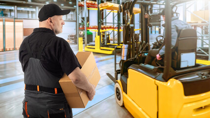 Man works in warehouse. Storage contractor with box. Man storekeeper near forklift. Guy in...