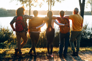 group of friends hiking in nature together - team standing at sunset in front lake water - vacation...