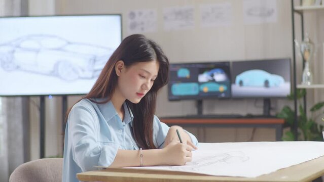 Asian Female Having A Headache While Working On A Car Design Sketch On Table In The Studio With Tv And Computers Display 3D Electric Car Model 
