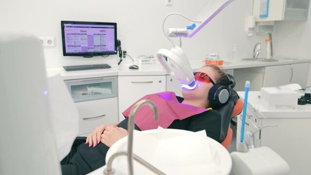 Patient wearing protective glasses during LED whitening sitting in a chair in the clinic. Photo-whitening of teeth in a modern dental clinic
