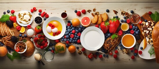 The breakfast food table is a festive brunch set with a variety of meals like granola, fried egg, pancakes, croissants, smoothie, fresh vegetables, berries and fruits. The view is overhead and space
