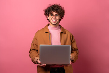 Studio portrait of young man standing holding laptop and looking at camera with happy smile