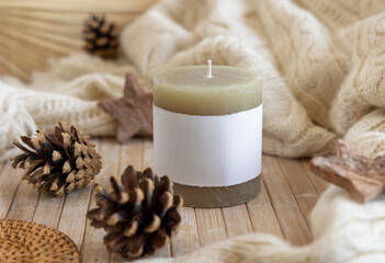 Fototapeta na wymiar Candle with blank label near pine cones and cream sweater, Close up, copy space, mock up