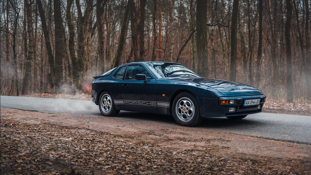 Dark blue Porsche 944 in autumn forest. Front three quarter view of 1980s sportscar. Kyiv, Ukraine - November 26 2017.
