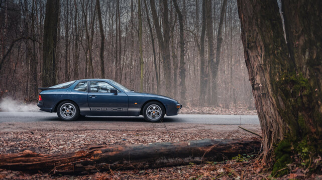 Dark blue Porsche 944 in autumn forest. Side profile view of 1980s sportscar. Kyiv, Ukraine - November 26 2017.