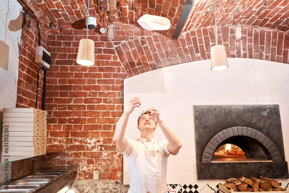 Wall mural the chef prepare pizza. raw pizza ready to bake. cook in a apron in the kitchen rolls out pizza doug