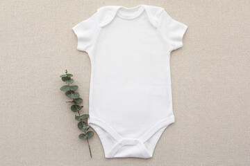 Baby onesie flat lay on a linen fabric with eucalyptus. Baby bodysuit mockup. Copy space for your design here. Top view. Flat Lay.