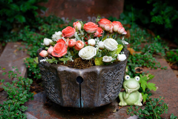 a brown pot with white and red artificial roses as grave decoration on a cemetery