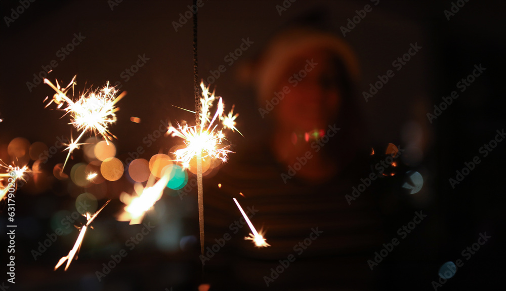 Wall mural Close-up of burning bengal lights. Smiling woman looking at sparkler with happiness and admiration on background. Happy New Year and Merry Christmas concept