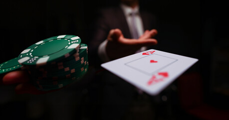 Close-up of man in presentable suit throwing playing card ace of hearts to opponent on dark background. Winning in business and risky avid player concept