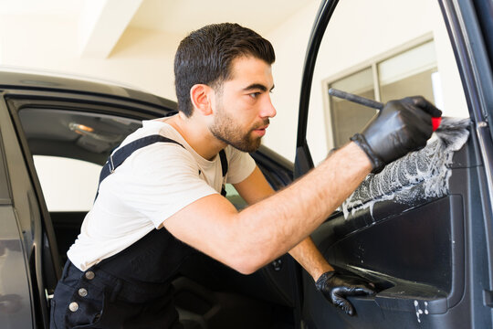 Young Mexican worker cleaning car door interior at workshop