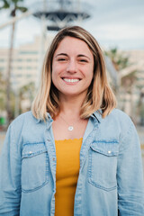 Vertical portrait of happy blonde young adult woman standing outside with friendly and optimistic expression. Caucasian beauty female with perfect white teeth smiling and looking satisfed at camera