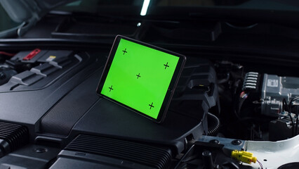 Unrecognizable male car service worker checking car and doing maintenance using a digital tablet computer with green screen chromakey, while standing near the opened bonnet © Vladislav