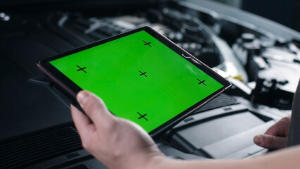 Unrecognizable male car service worker checking car and doing maintenance using a digital tablet computer with green screen chromakey, while standing near the opened bonnet