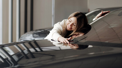 
smiling beautiful woman hugging her new car in a car dealership. young woman fulfills her dream,...