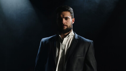 Portrait of a bearded man sitting with a serious face, against a dark background.