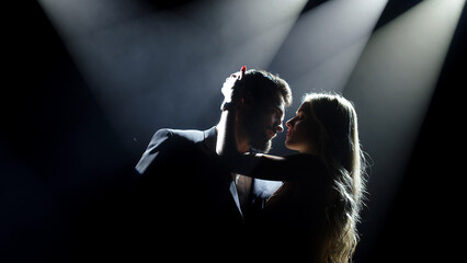 Silhouette of sensual lovers, woman hugs in the dark. Romantic couple touch each other on the background of spotlights. Sexy man and woman.