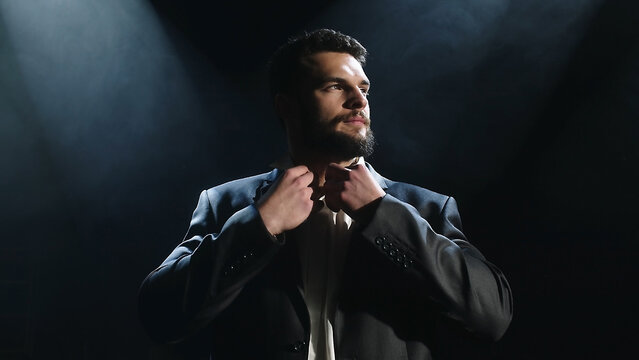 Portrait of a bearded man sitting with a serious face, against a dark background.