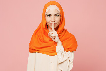 Young arabian asian muslim woman wear orange abaya hijab say hush be quiet with finger on lips shhh...