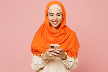 Young smiling happy arabian asian muslim woman wears orange abaya hijab hold in hand use mobile...