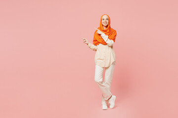 Full body smiling happy fun young arabian asian muslim woman wearing orange abaya hijab point index...