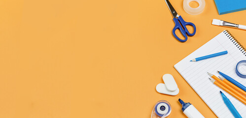 Assorted office and school white and blue stationery on bright yellow background. Organized knolling for back to school or education and craft concept. Selective focus. Copy space banner