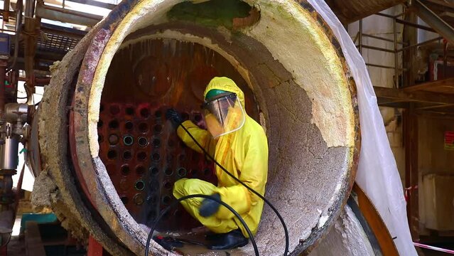 Male workers use high-pressure water jets to clean splashing the dirt of tube boilers in industrial areas, chemical products, or toxic hazardous material sulfur