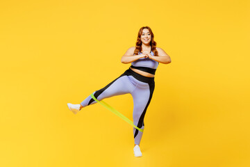 Fototapeta na wymiar Full body young chubby plus size big fat fit woman wear blue top warm up train use rubber elastic bands for legs look camera isolated on plain yellow background studio home gym. Workout sport concept.
