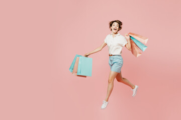 Full body young overjoyed happy woman wearing casual clothes hold shopping paper package bags run fast looking camera isolated on plain pink color background studio. Black Friday sale buy day concept.