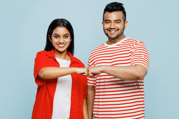 Young smiling happy couple two friends family Indian man woman wearing red casual clothes t-shirts together look camera give fistbump gesture isolated on pastel plain light blue cyan color background.