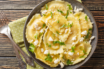 Homemade pasta mezzaluna stuffed with goat cheese and herbs close-up in a plate on the table. Horizontal top view from above