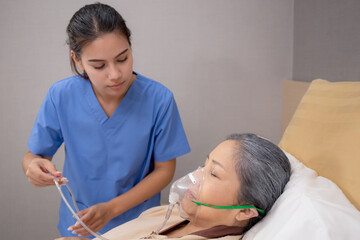 Fototapeta premium Nurse putting oxygen mask with patient elderly woman on bed for diagnose and healing in hospital, specialist doctor giving oxygen mask with senior emergency for recovery in clinic, medical concept.
