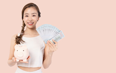 Happy young Asian woman show crash and hold piggy bank for saving money She become rich person because spend money economically Pretty Young girl holding piggy bank isolated on pink background 