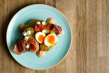 Avocado toast with guacamole, soft boiled egg, ham, cream cheese and tomatoes on a plate