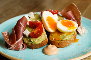 Avocado toast with guacamole, soft boiled egg, ham, cream cheese and tomatoes on a plate