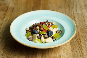 A bowl of cereal with fruits on a wooden table