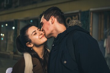Fototapeta premium Young caucasian man kissing his girlfriend on the street at night