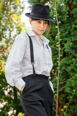 Beautiful girl with a hat, in a white shirt, in black trousers with suspenders