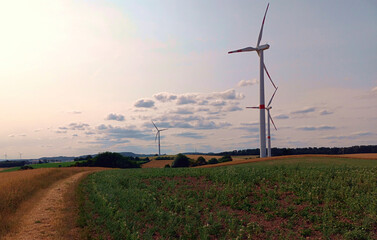 Windenergie: Windräder in der Natur zwischen Wiesen und Feldern bei leicht bewölktem Himmel bei...