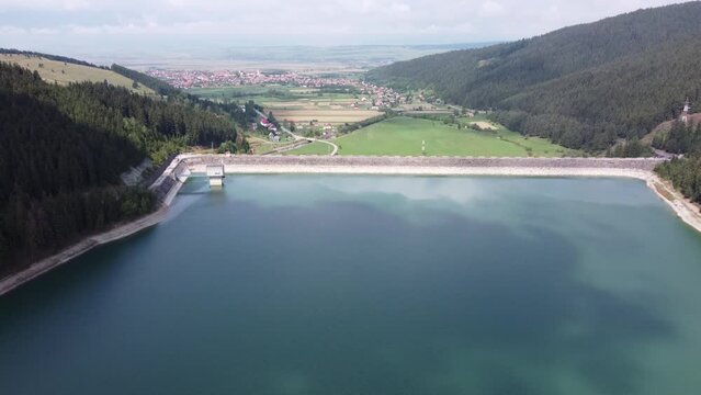 Aerial footage over Lake Barajul Frumoasa and a nearby village surrounded by green forests